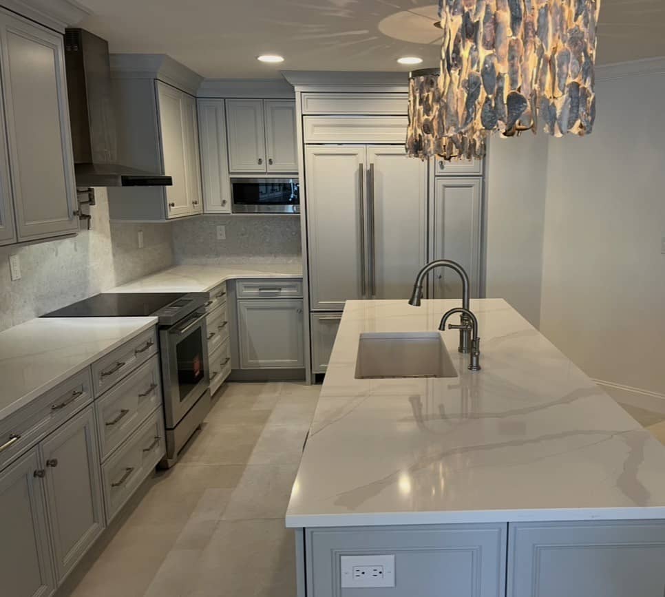 Gray painted kitchen with a waterfall-edge quartz island, an oyster-shell chandelier, a mosaic tile backsplash, and a window over the sink.